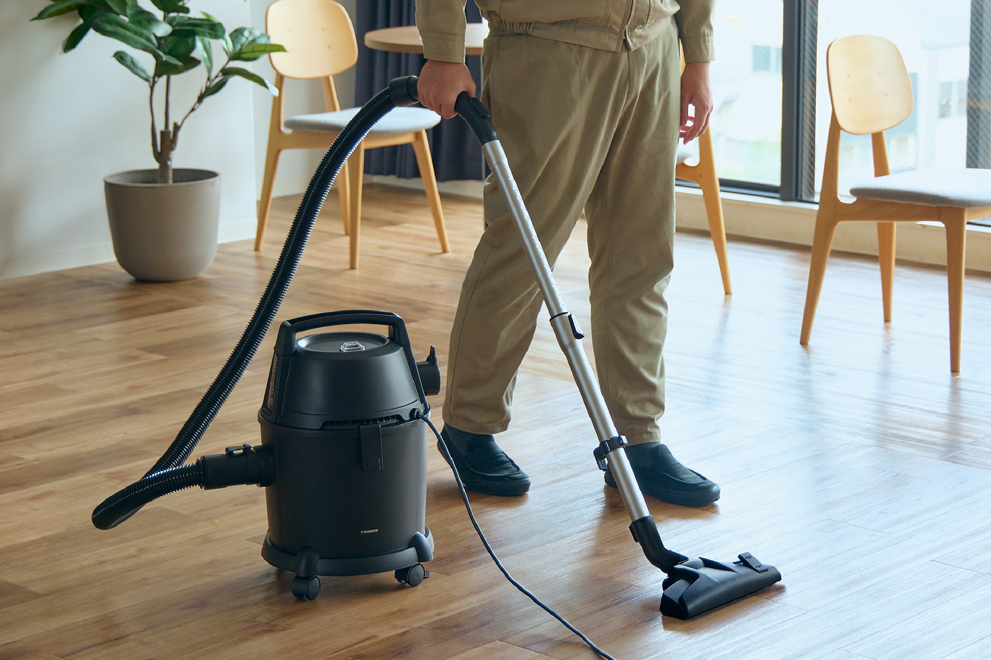 作業着を着た男性が乾湿両用クリーナーで室内を掃除している写真